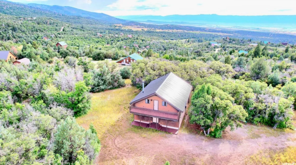 Aerial view of property and surrounding area featuring a mountainous background and a heavily wooded area
