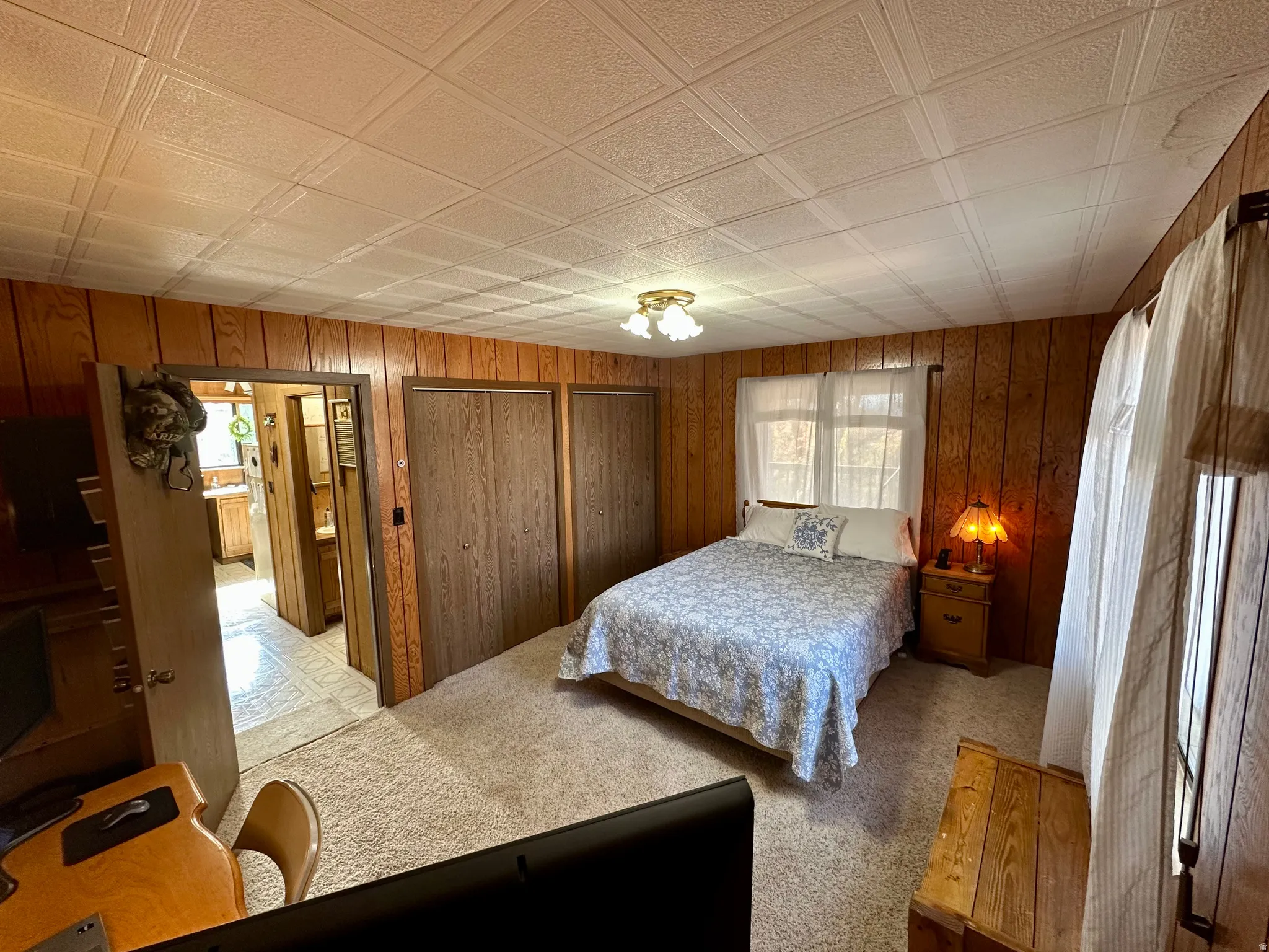 Bedroom with an ornate ceiling, light colored carpet, wood walls, and multiple closets