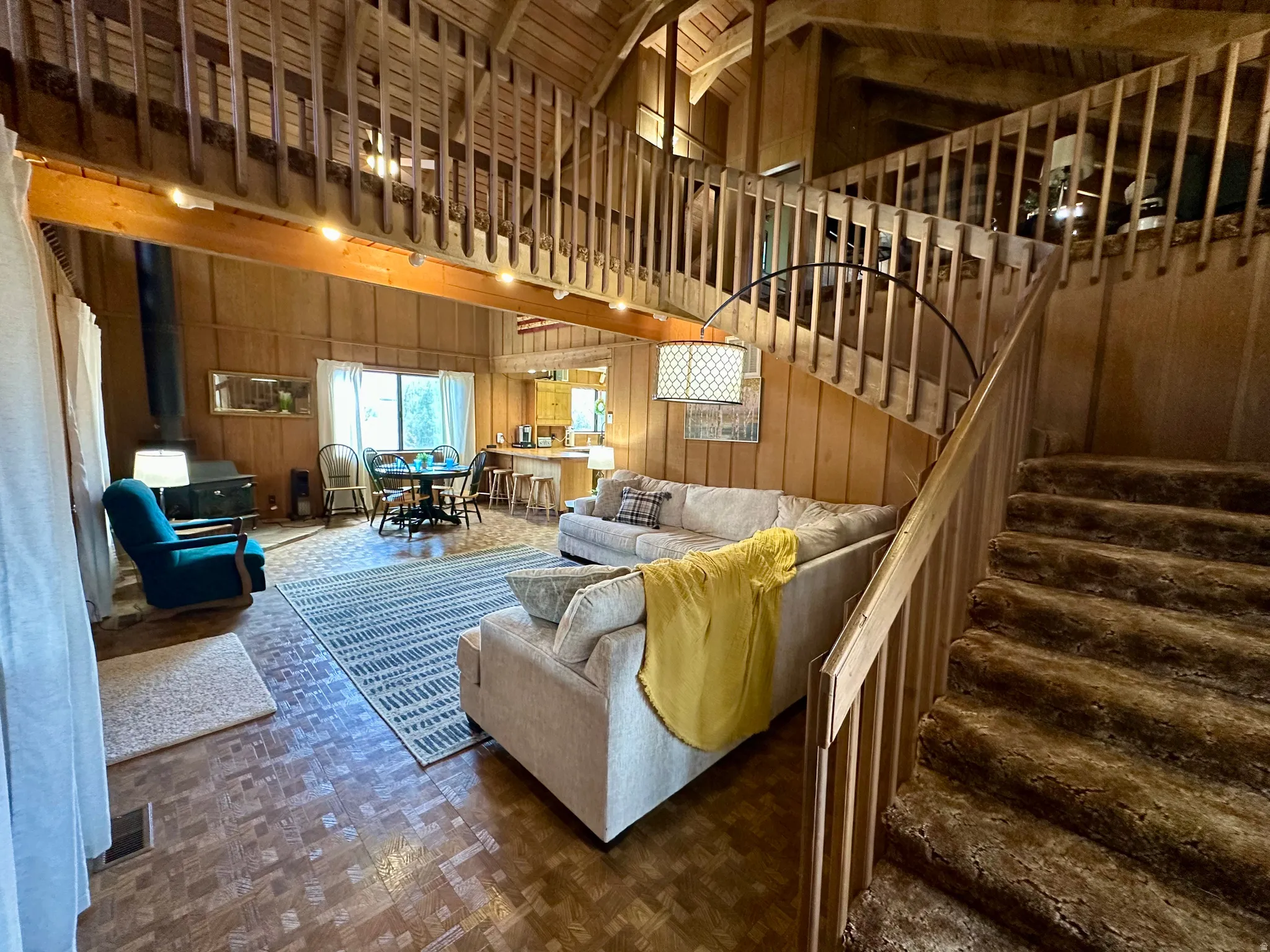 Living room with wood walls, parquet flooring, vaulted ceiling, and a wood stove