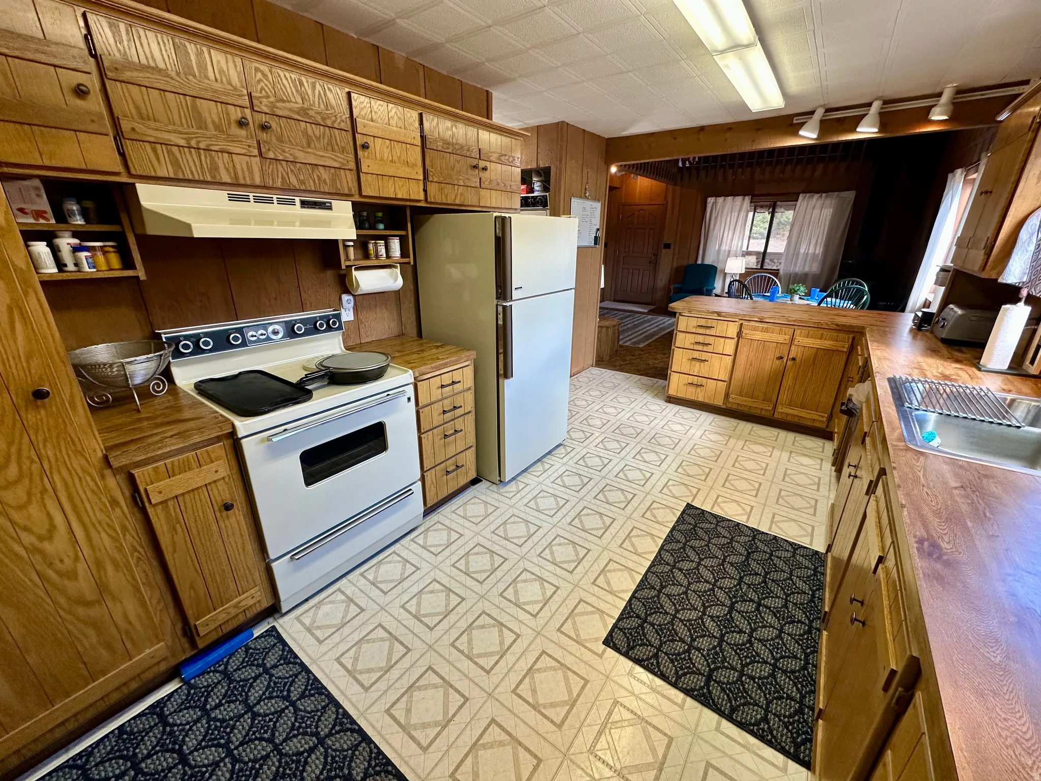 Kitchen featuring white appliances, wood finish cabinets, a peninsula, light flooring, and wooden walls