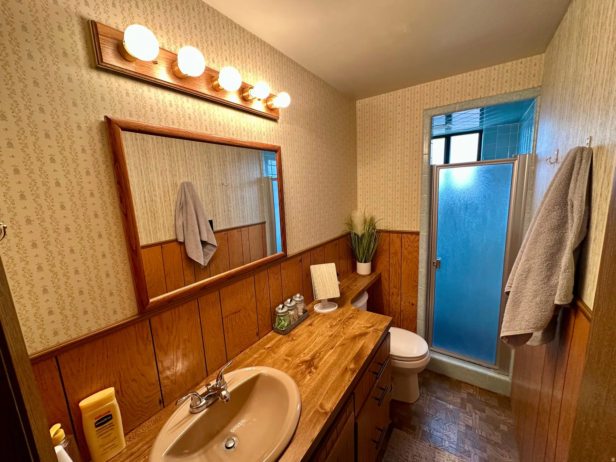 Full bath featuring a shower stall, vanity, wood walls, and wainscoting