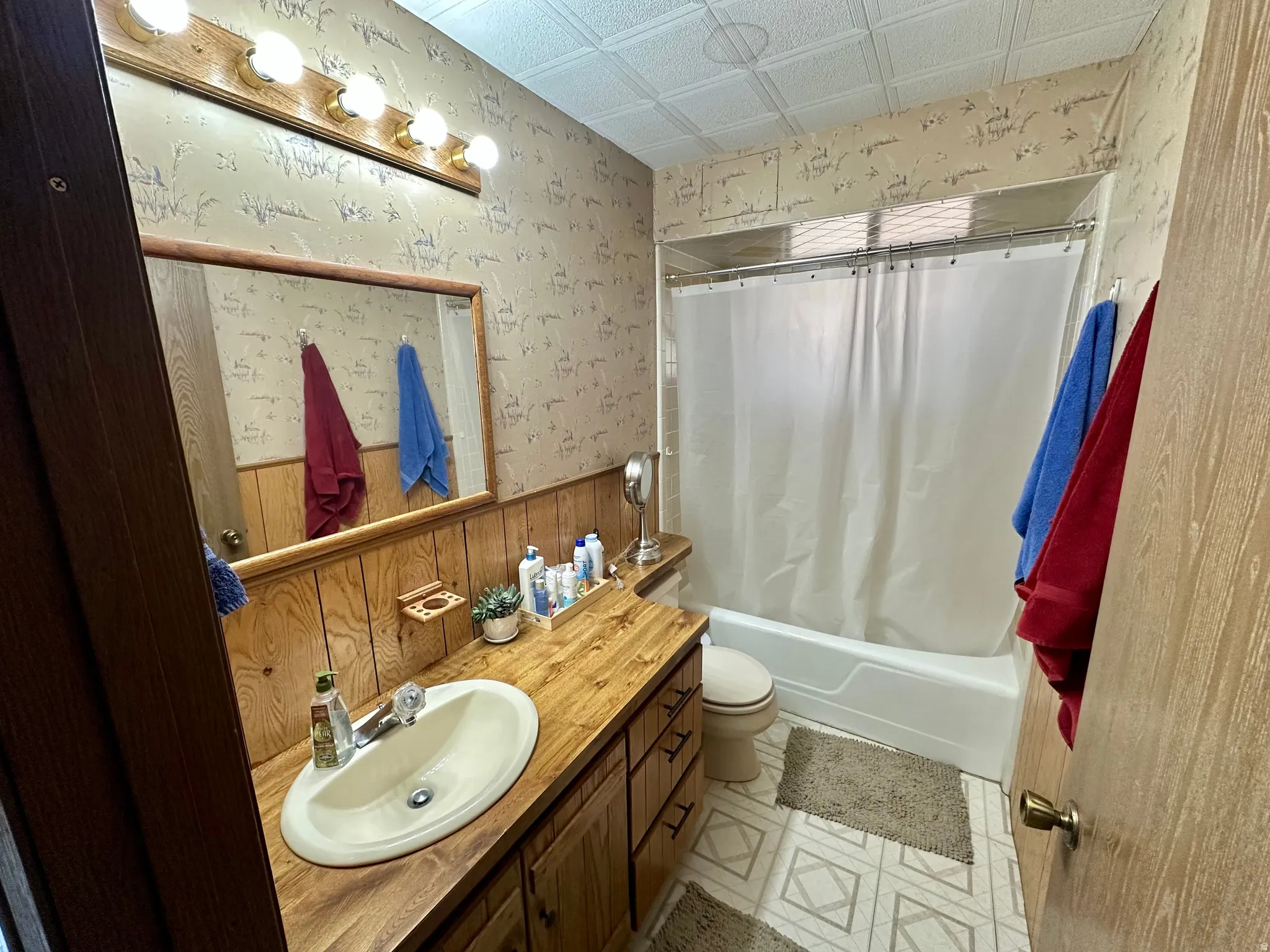 Bathroom featuring wallpapered walls, vanity, an ornate ceiling, shower / tub combo with curtain, and wainscoting