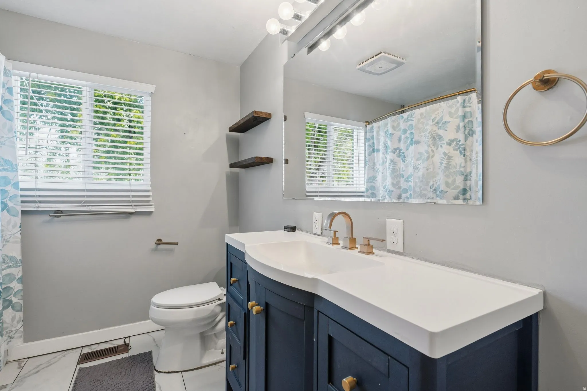 Bathroom featuring a navy blue vanity with gold hardware, integrated white sink, and gold-finish faucet