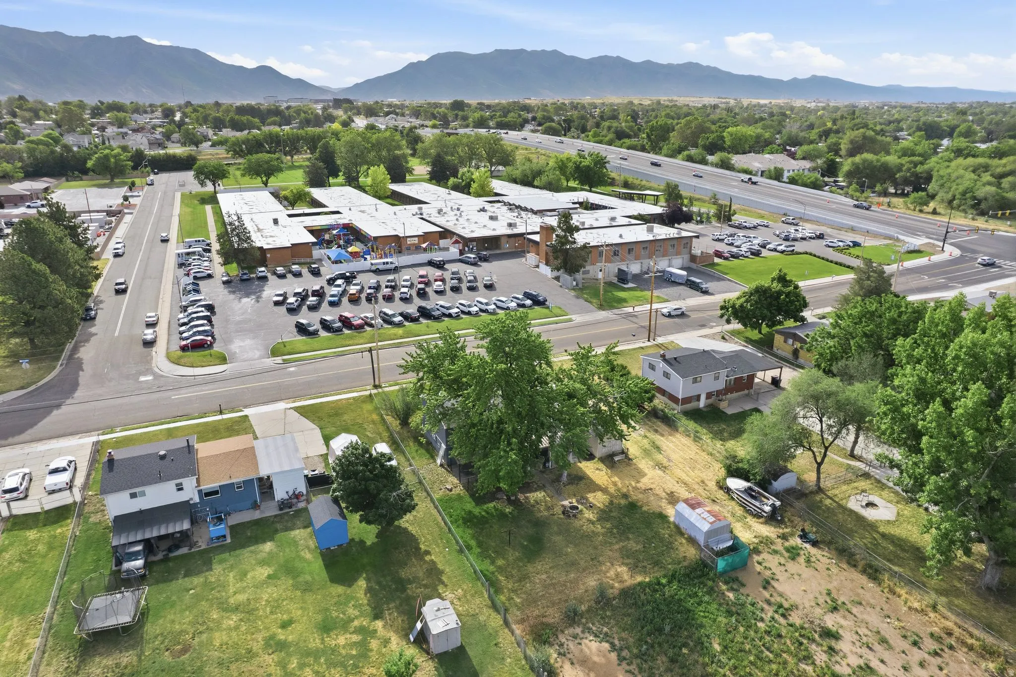 Aerial perspective showcasing a commercial property with extensive parking, a multi-lane highway, and distant mountain ranges
