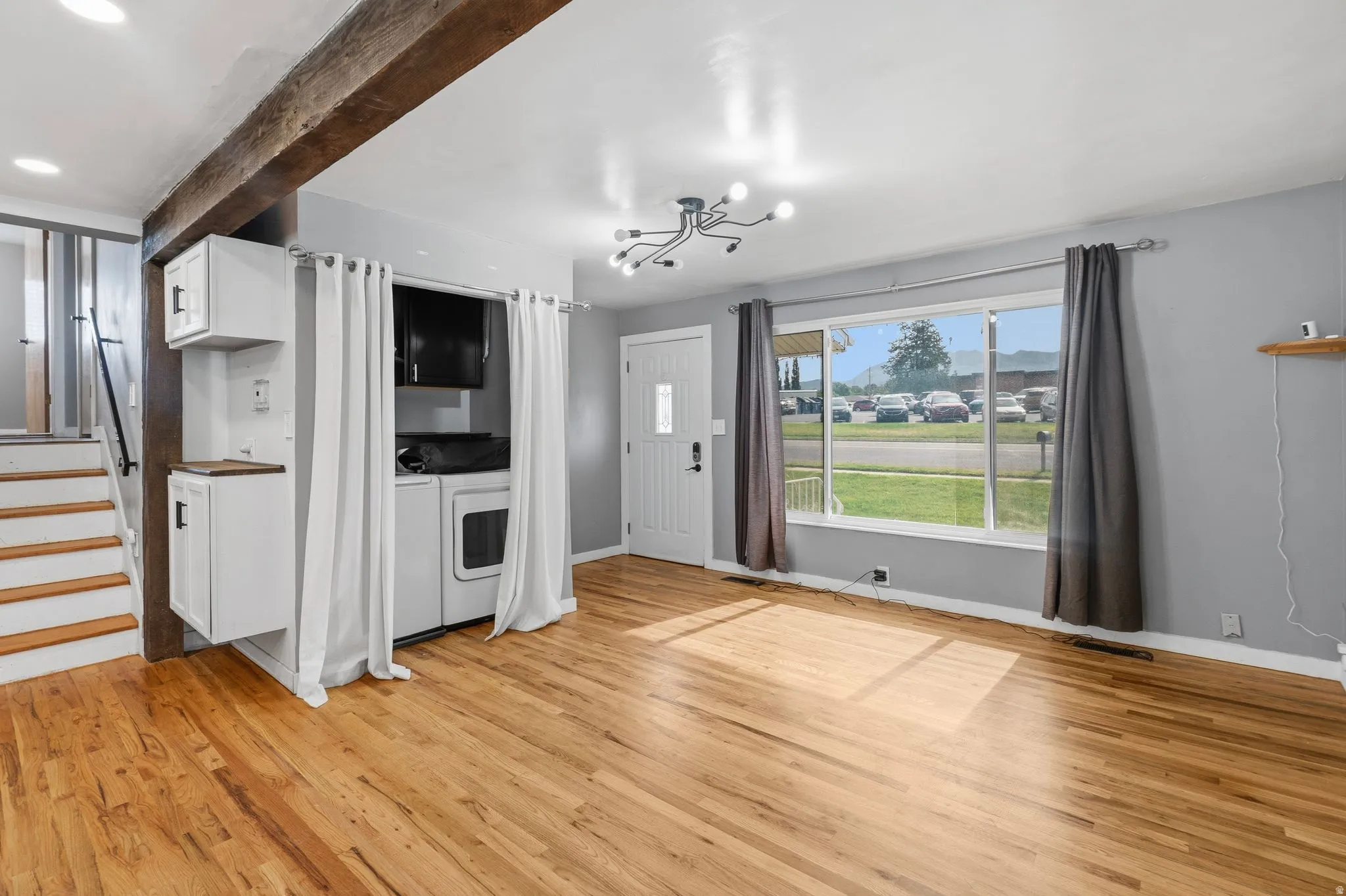 Spacious room featuring wood-finish flooring, a contemporary light fixture, and a large front window