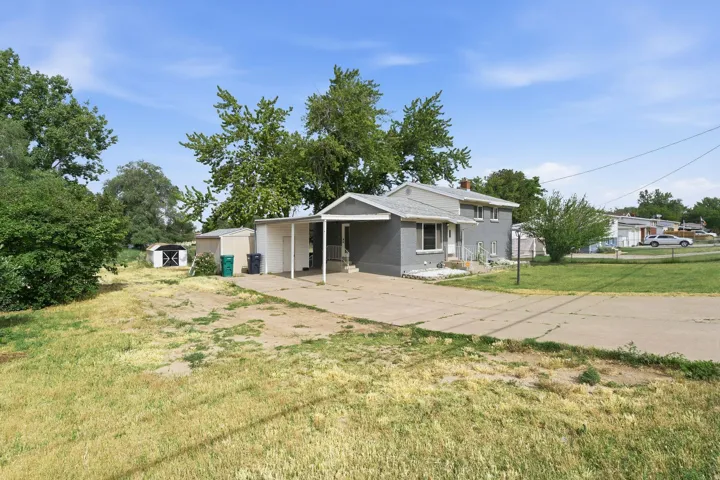 Gray exterior home with a partial covered porch, featuring a gravel driveway and a detached storage shed