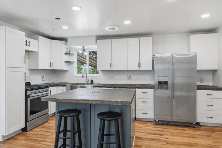 Kitchen featuring white cabinetry with black hardware, stainless steel appliances, wood-finish flooring, recessed lighting, and a kitchen island with seating