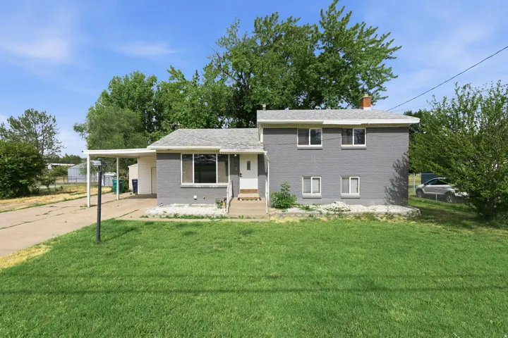 Gray brick exterior with white trim, featuring a single entry door and an attached carport