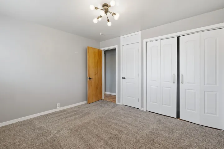 Carpeted room featuring light gray walls, a modern sputnik-style ceiling light, a natural wood-finish interior door, and white bi-fold closet doors