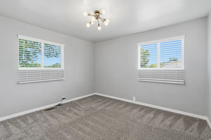 Room featuring two windows with white blinds, gray textured carpet, light gray wall paint, and a modern sputnik-style ceiling light fixture