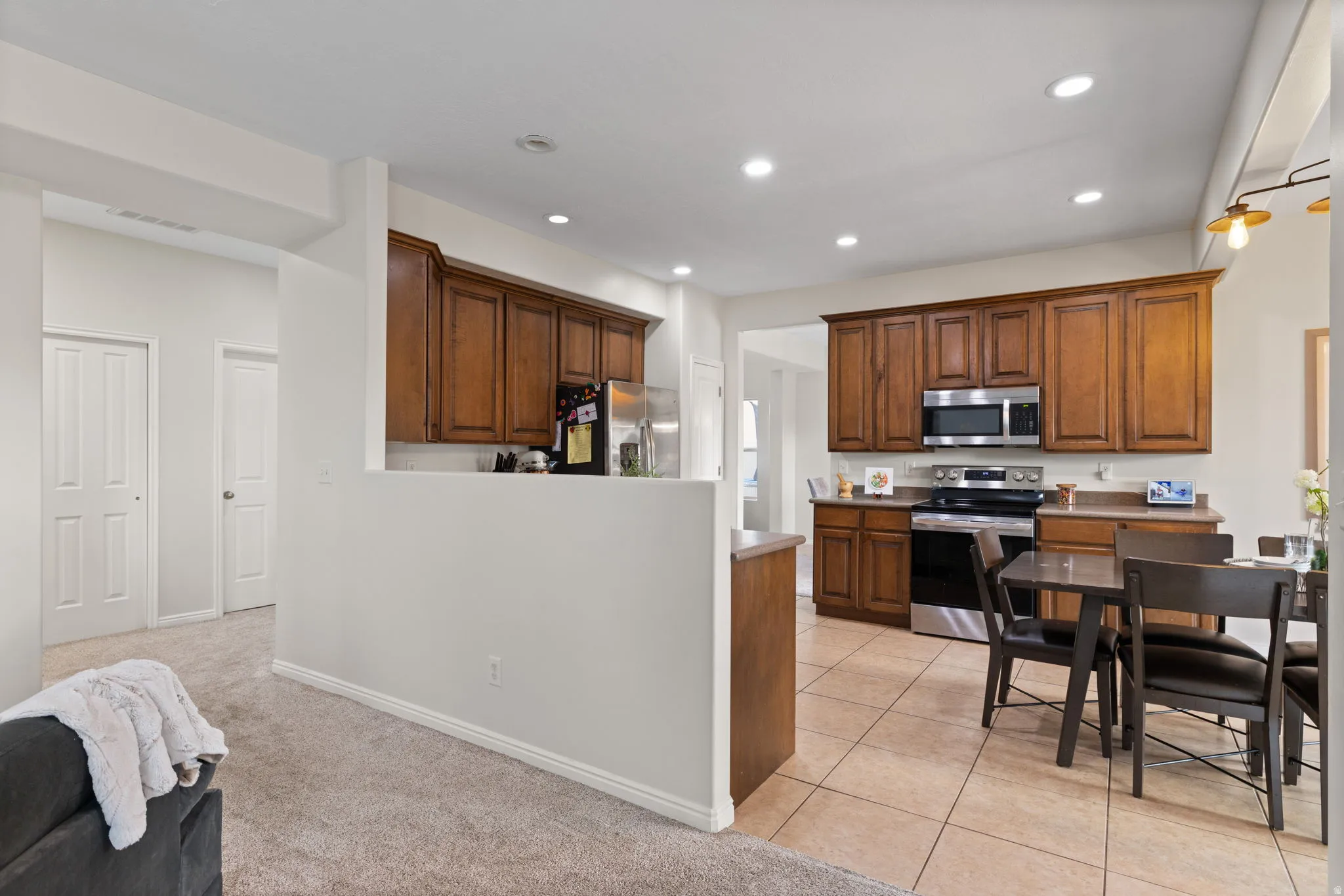 Kitchen featuring stainless steel appliances, light carpet, light tile patterned floors, wood finish cabinetry, and a peninsula