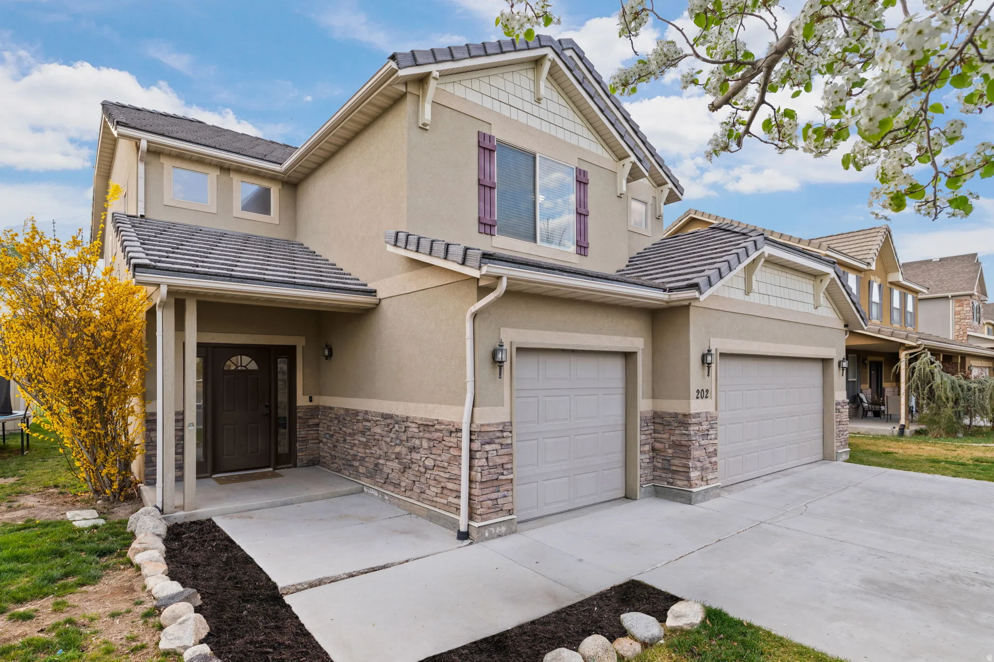 Stucco exterior with stone accenting, featuring a covered entry, two-car garage, and shuttered windows