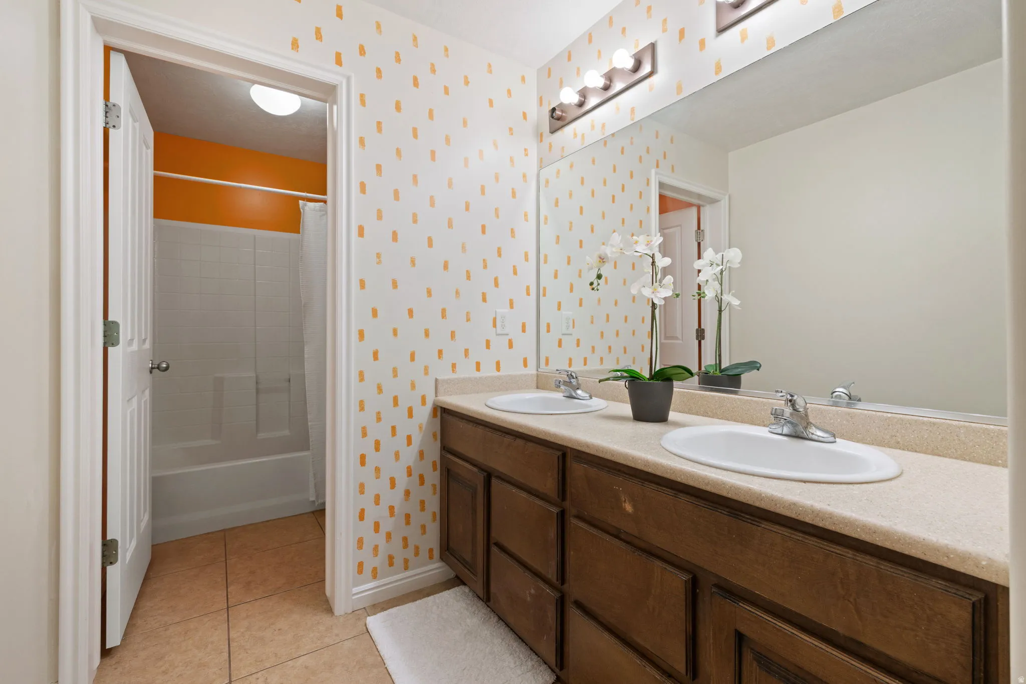 Bathroom with wallpapered walls, double vanity, light tile patterned floors, and shower / bathtub combination with curtain