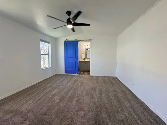 Unfurnished bedroom featuring a ceiling fan, dark carpet, ensuite bath, and lofted ceiling
