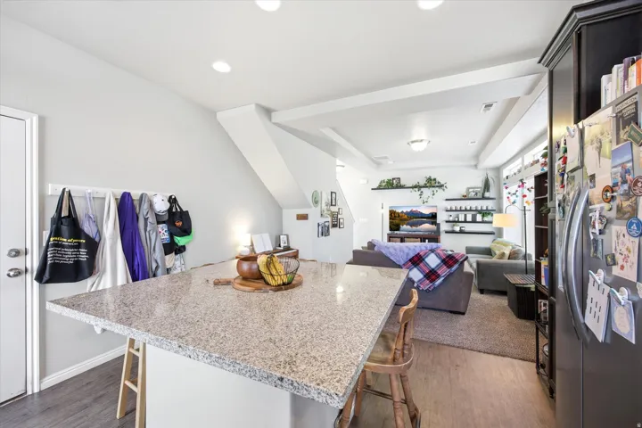 Kitchen featuring a breakfast bar area, freestanding refrigerator, dark wood finished floors, light stone countertops, and a center island