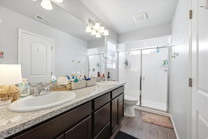 Bathroom with double vanity, a stall shower, and dark wood finished floors