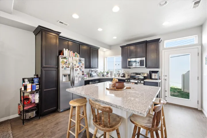 Kitchen with a kitchen bar, dark wood finish cabinetry, stainless steel appliances, light stone counters, and dark wood-style flooring