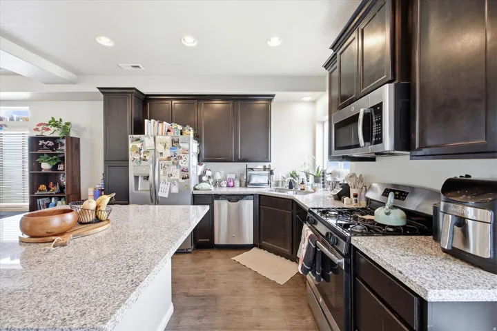 Kitchen featuring stainless steel appliances, dark wood finish cabinets, light stone counters, recessed lighting, and dark wood-style floors