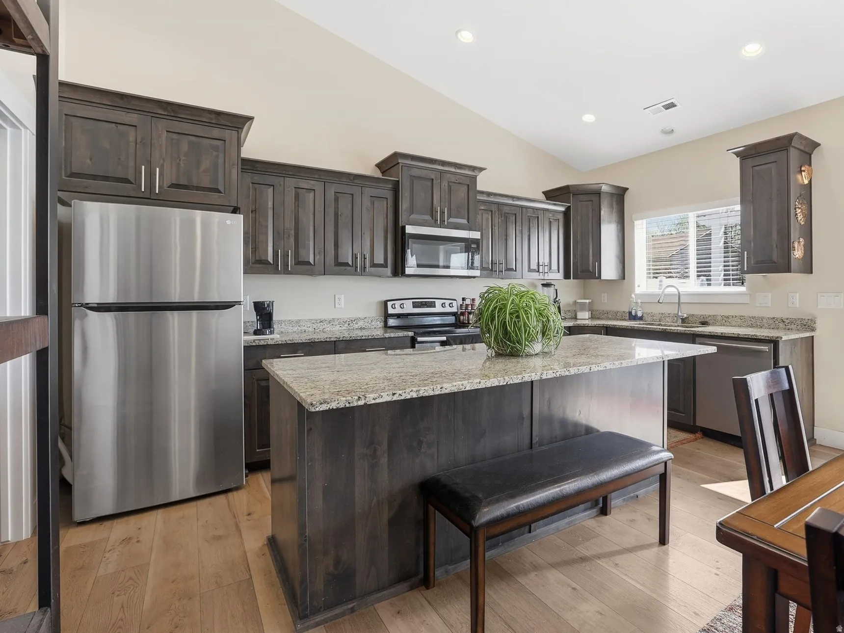 Kitchen with stainless steel appliances, dark wood finish cabinets, light stone counters, a kitchen island, and light wood finished floors