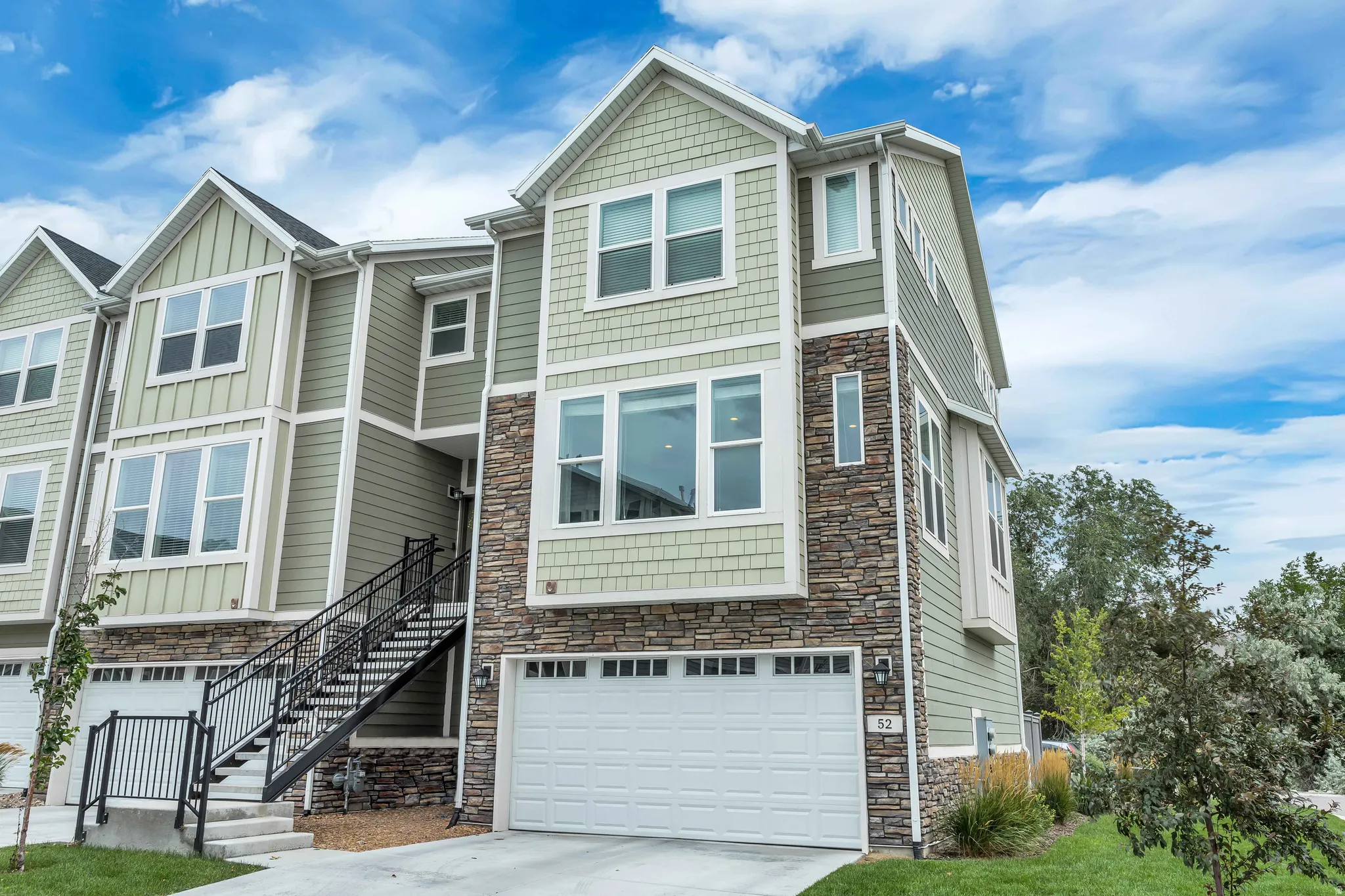Craftsman-style row-end townhome featuring stone siding, a garage, driveway, and board and batten siding