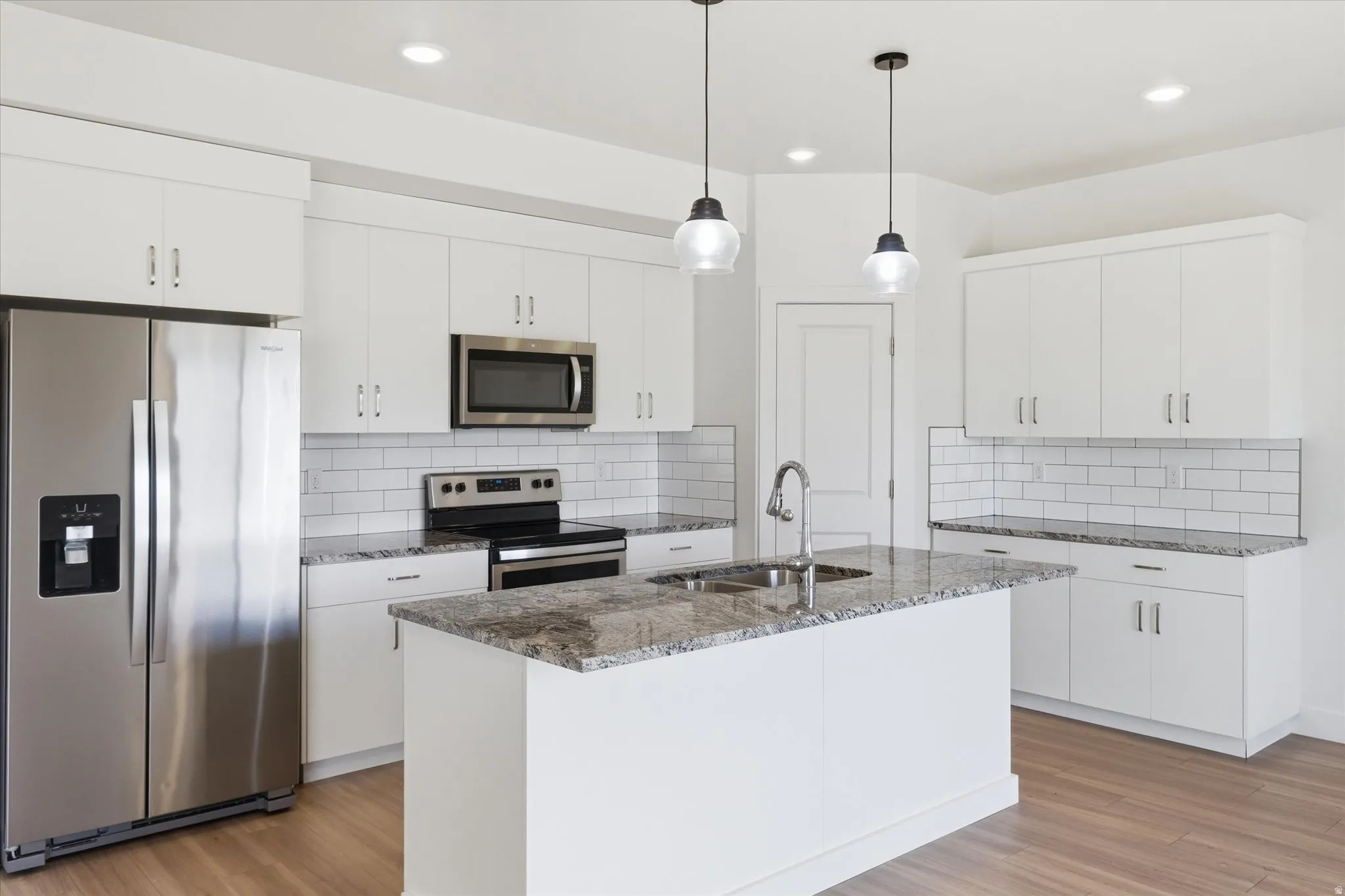 Kitchen with stainless steel appliances, dark stone counters, light wood finished floors, decorative backsplash, and white cabinetry