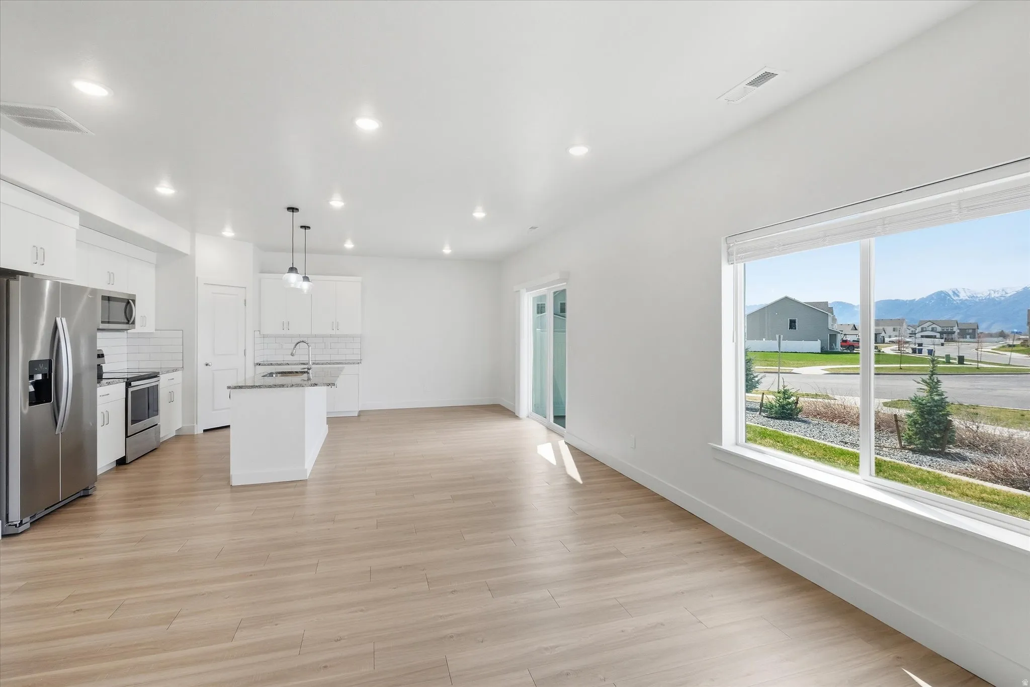 Kitchen with stainless steel appliances, white cabinetry, light wood-style flooring, a mountain view, and a center island with sink