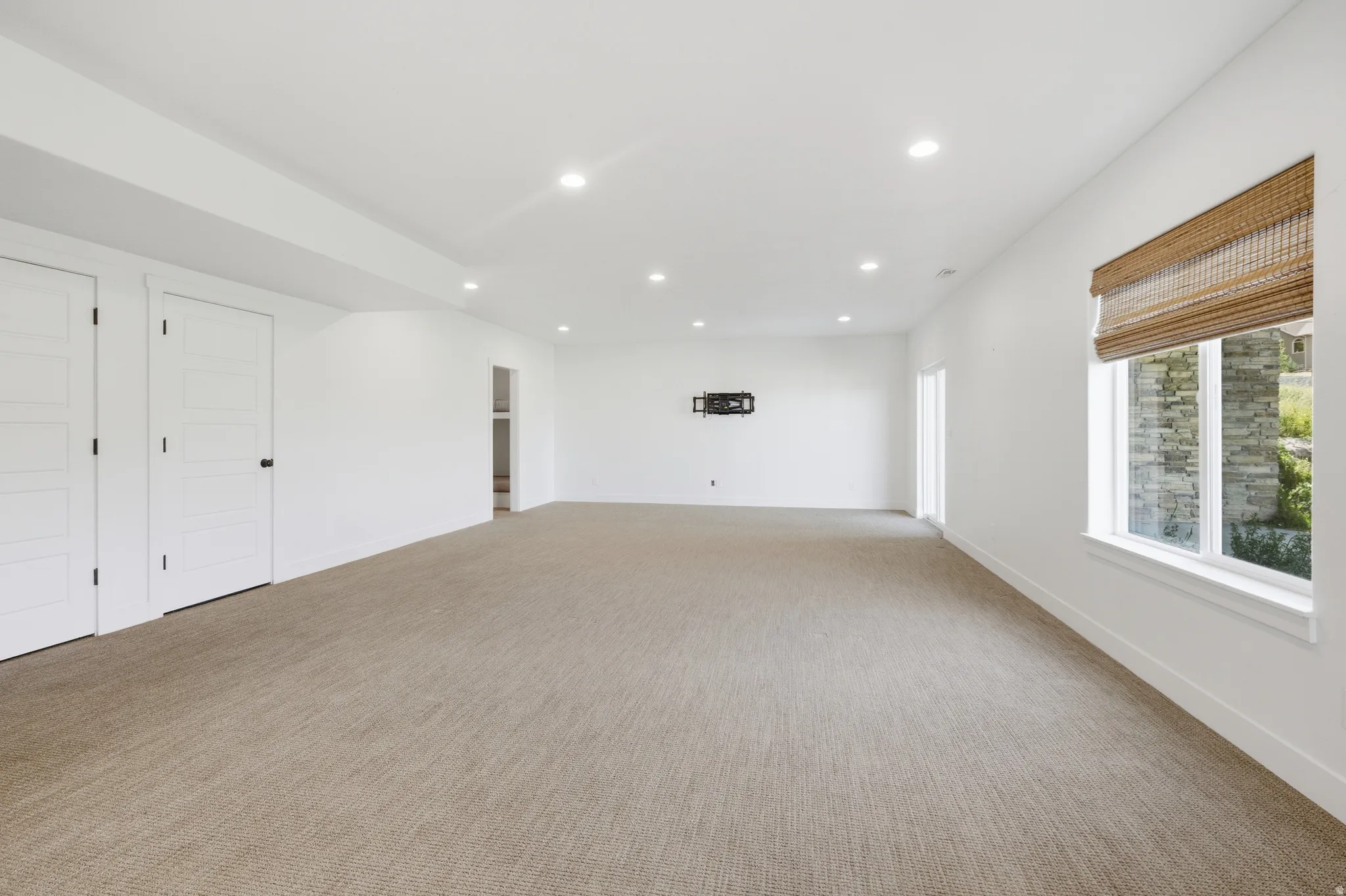 Spacious room featuring neutral carpeting, recessed lighting, white walls, and a window with a natural woven shade