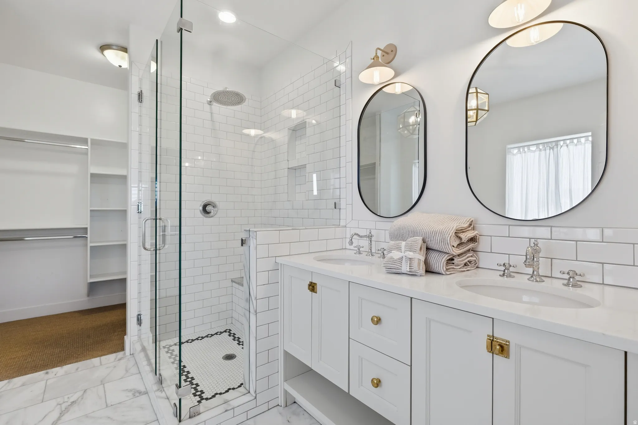Bathroom featuring a dual vanity with white cabinetry and brass hardware, two oval framed mirrors, and chrome fixtures