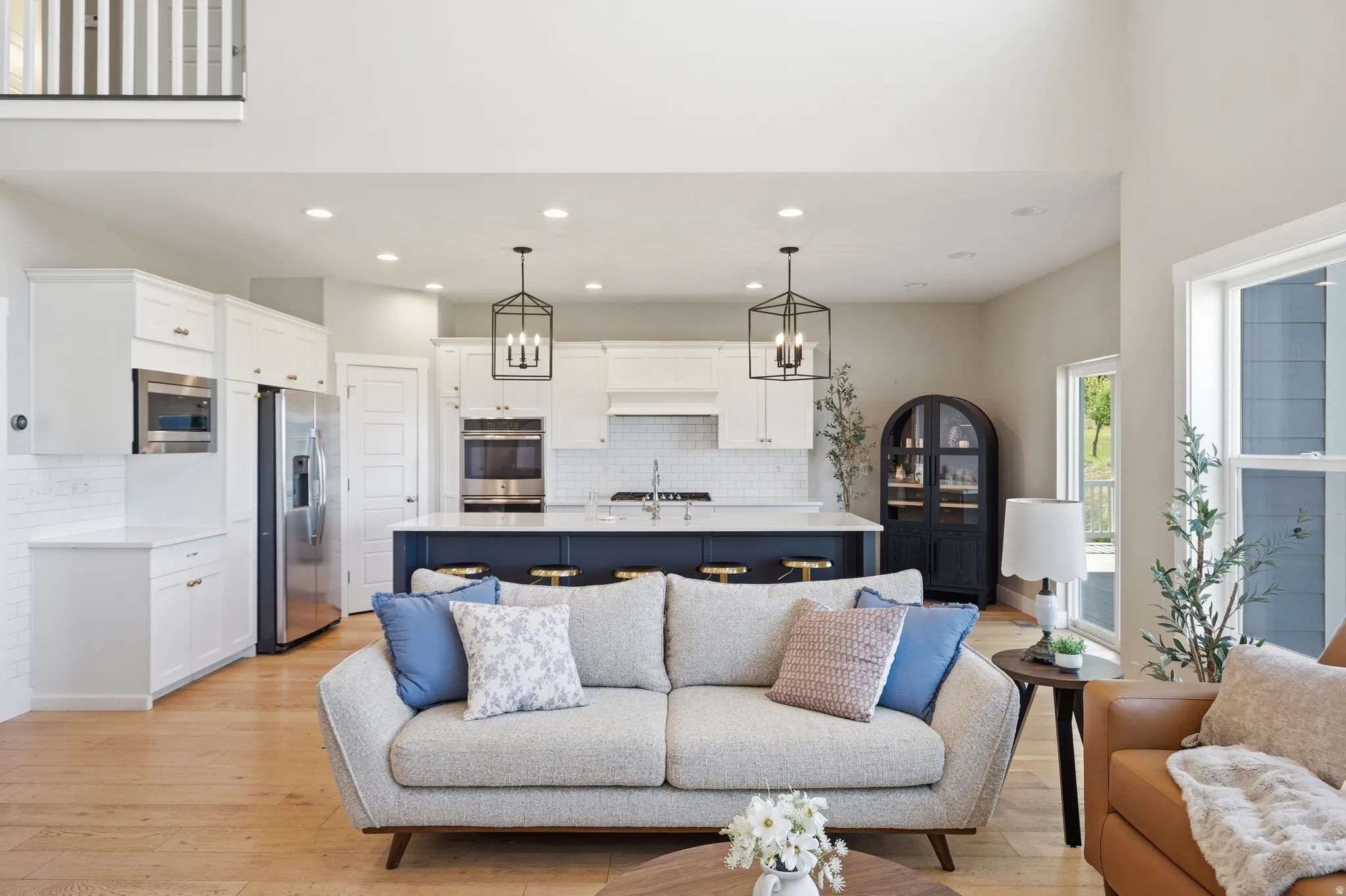 Open-concept living space featuring wood-finish flooring, recessed lighting, and a kitchen with white cabinetry, a blue island, and stainless steel appliances