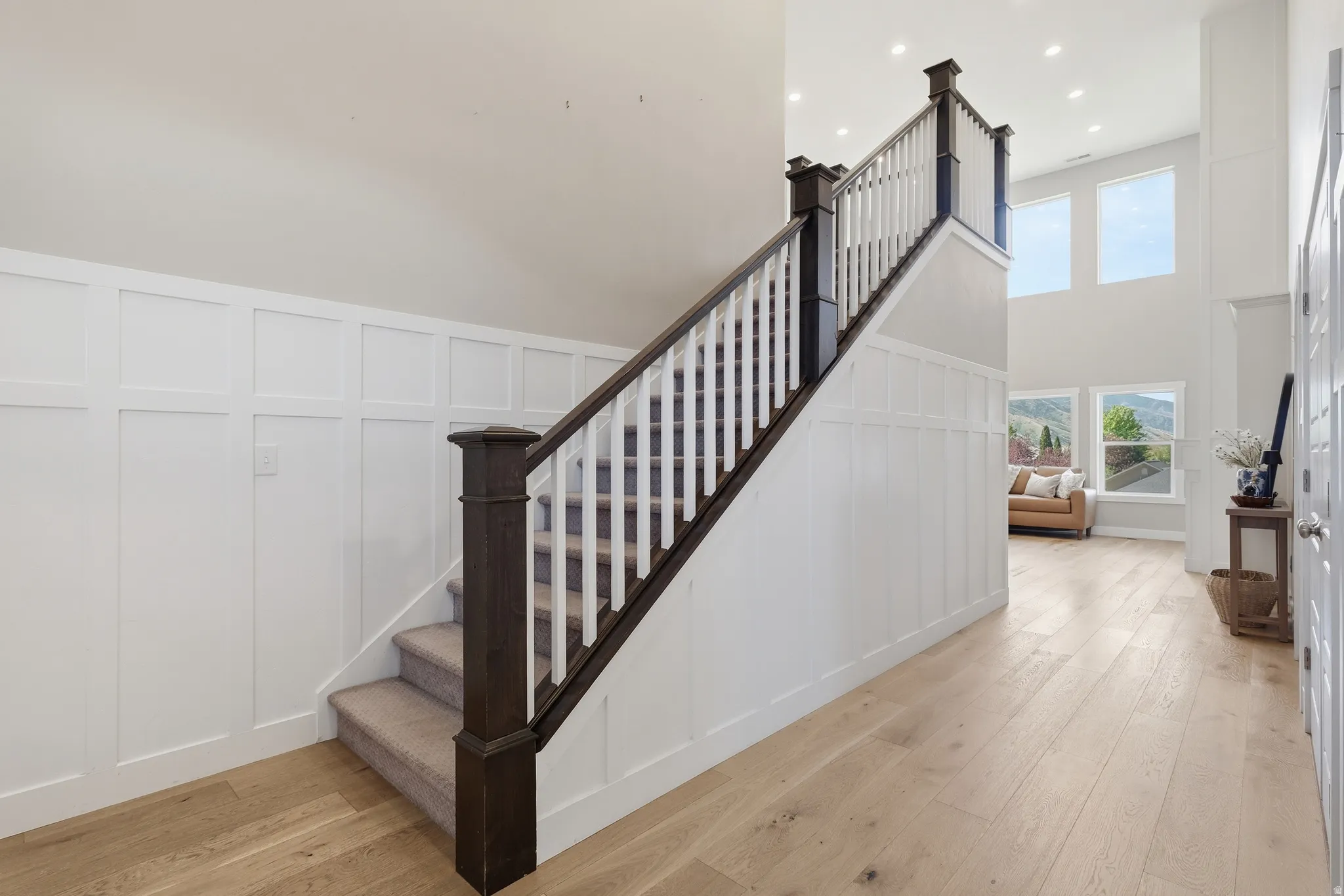 Two-story entryway featuring wood-finish flooring, a carpeted staircase with dark wood newel posts and handrail, white balusters, and board and batten wall detailing