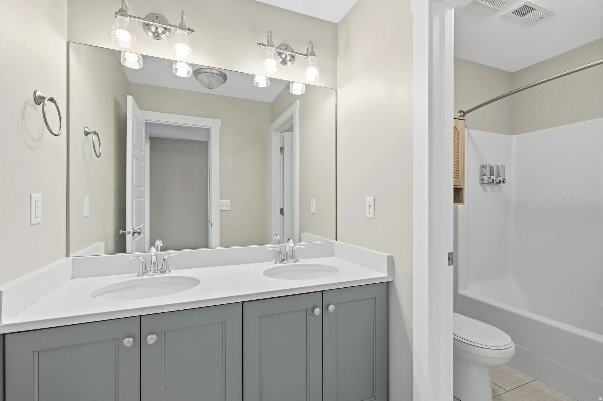 Bathroom featuring a dual vanity with a white countertop and gray cabinetry, brushed nickel hardware, and a large wall-mounted mirror