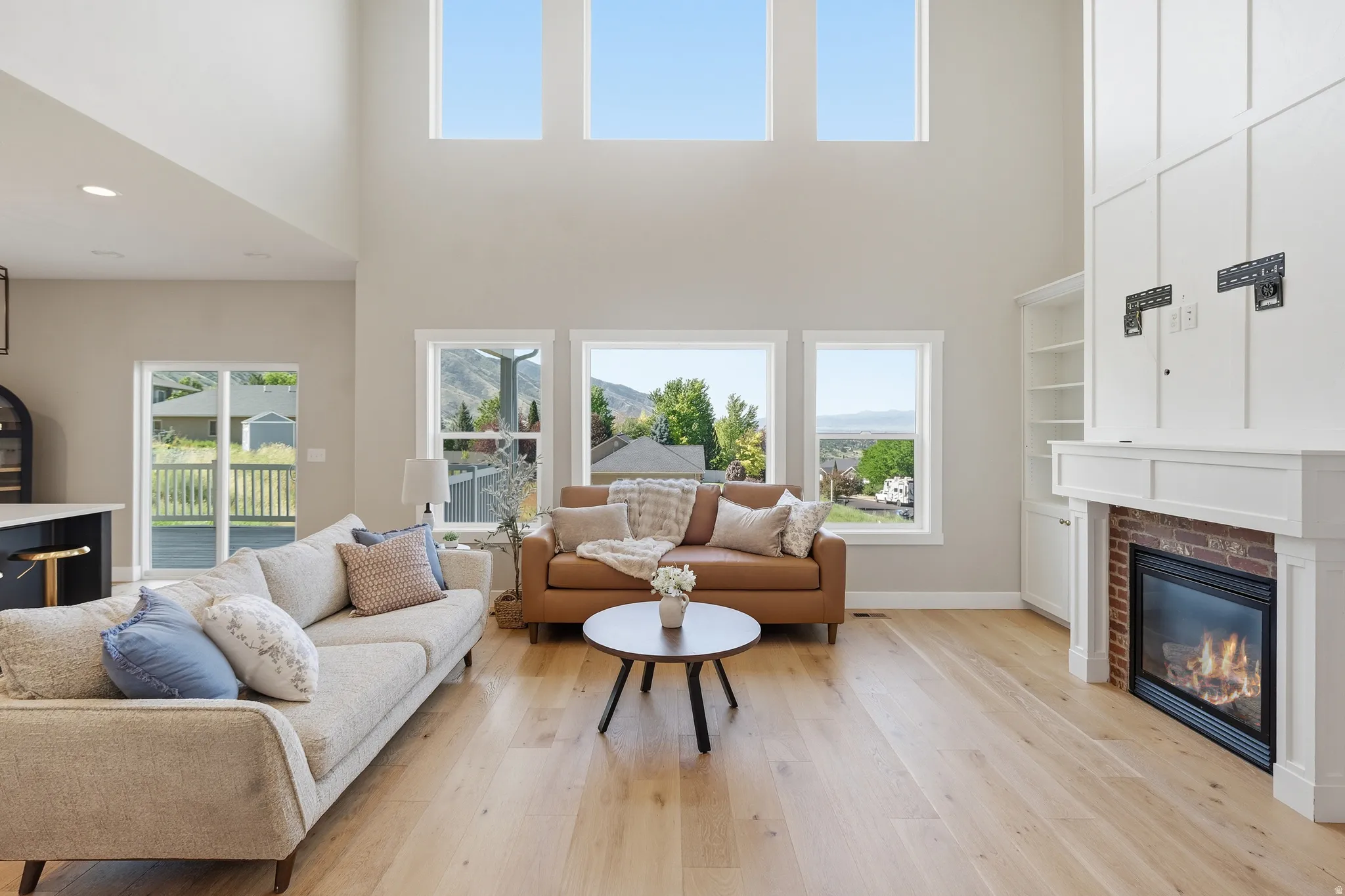 Spacious living area featuring high ceilings, wood-finish flooring, a fireplace with brick surround, built-in shelving, and large windows