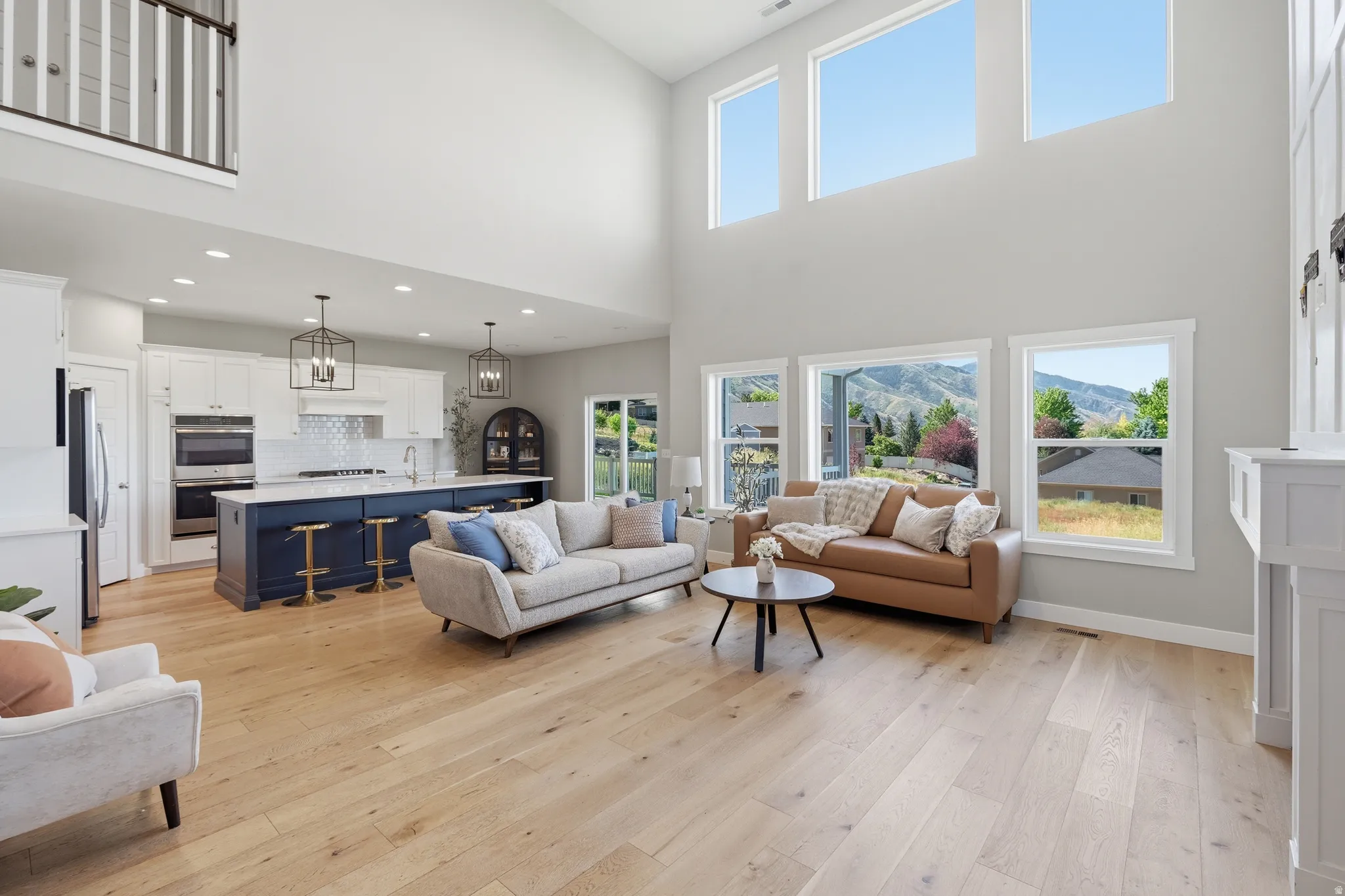 Two-story living area featuring wood-finish flooring, a white fireplace surround, and high ceilings with upper windows