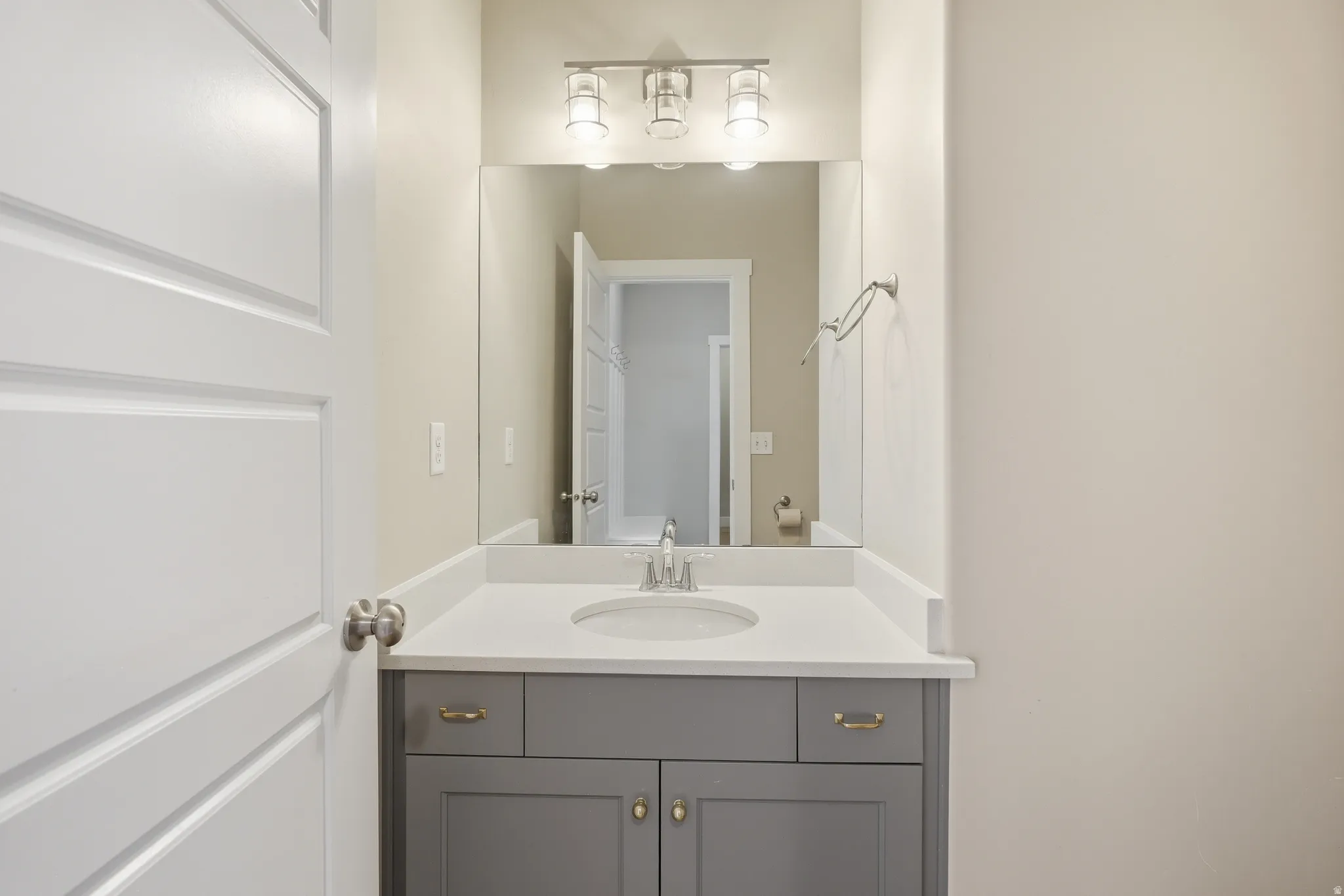 Bathroom vanity featuring a light gray cabinet with gold-toned hardware, an undermount sink, and a white countertop