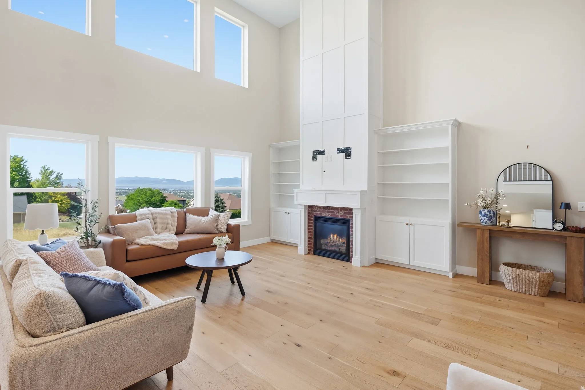 Spacious living area featuring high ceilings, light wood-finish flooring, and a fireplace with a brick surround