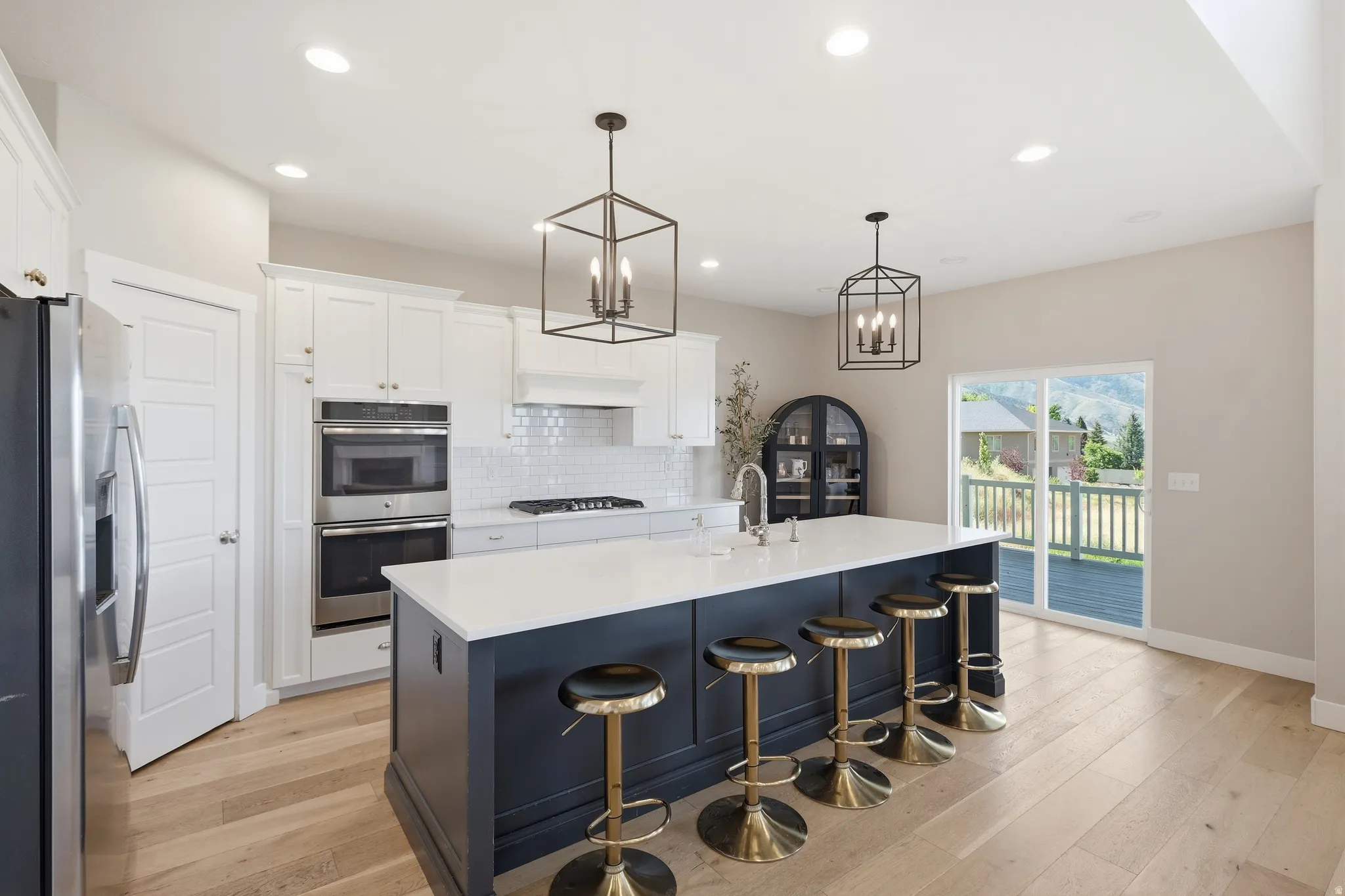 Kitchen featuring a large island with seating, integrated double ovens, white shaker cabinetry, and wood-finish flooring