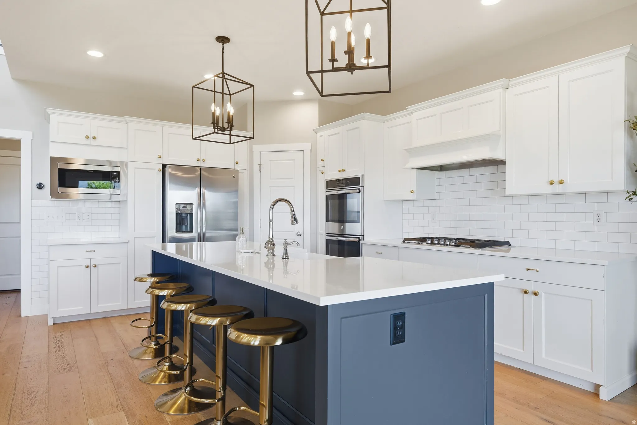 Modern kitchen featuring an expansive center island with seating, white shaker cabinetry, stainless steel appliances, and a subway tile backsplash