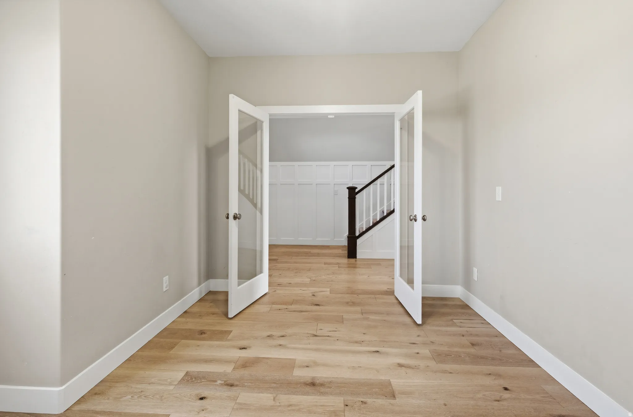 French doors featuring glass panels open to a room with wood-finish flooring, light neutral-toned walls, and white trim