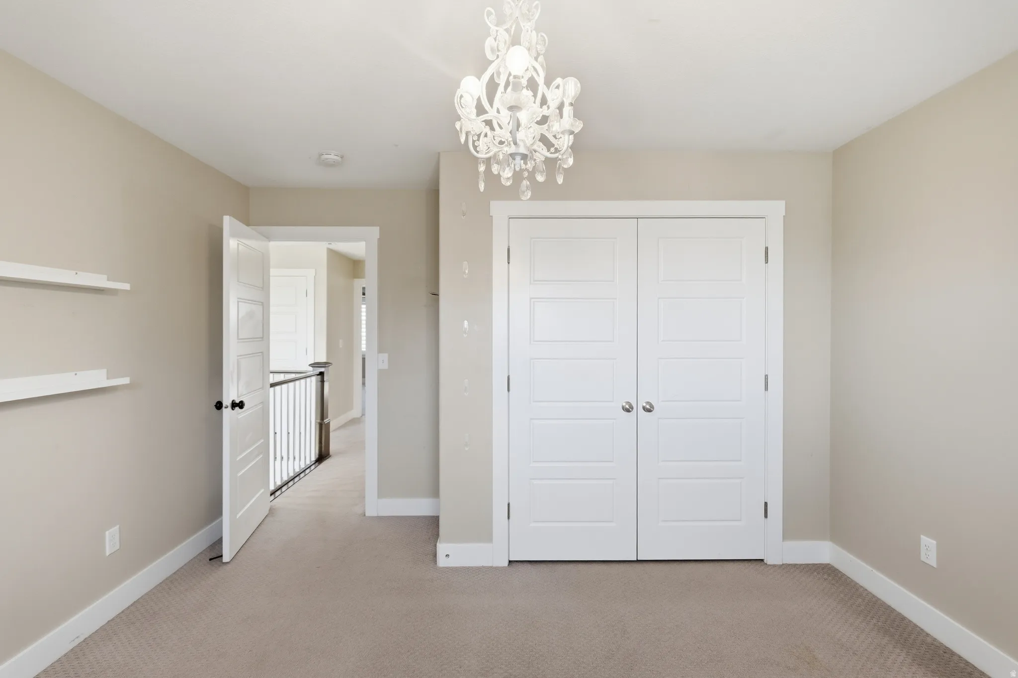 Room featuring plush carpeting, neutral wall tones, a decorative chandelier, white trim, and a double-door closet with modern paneling