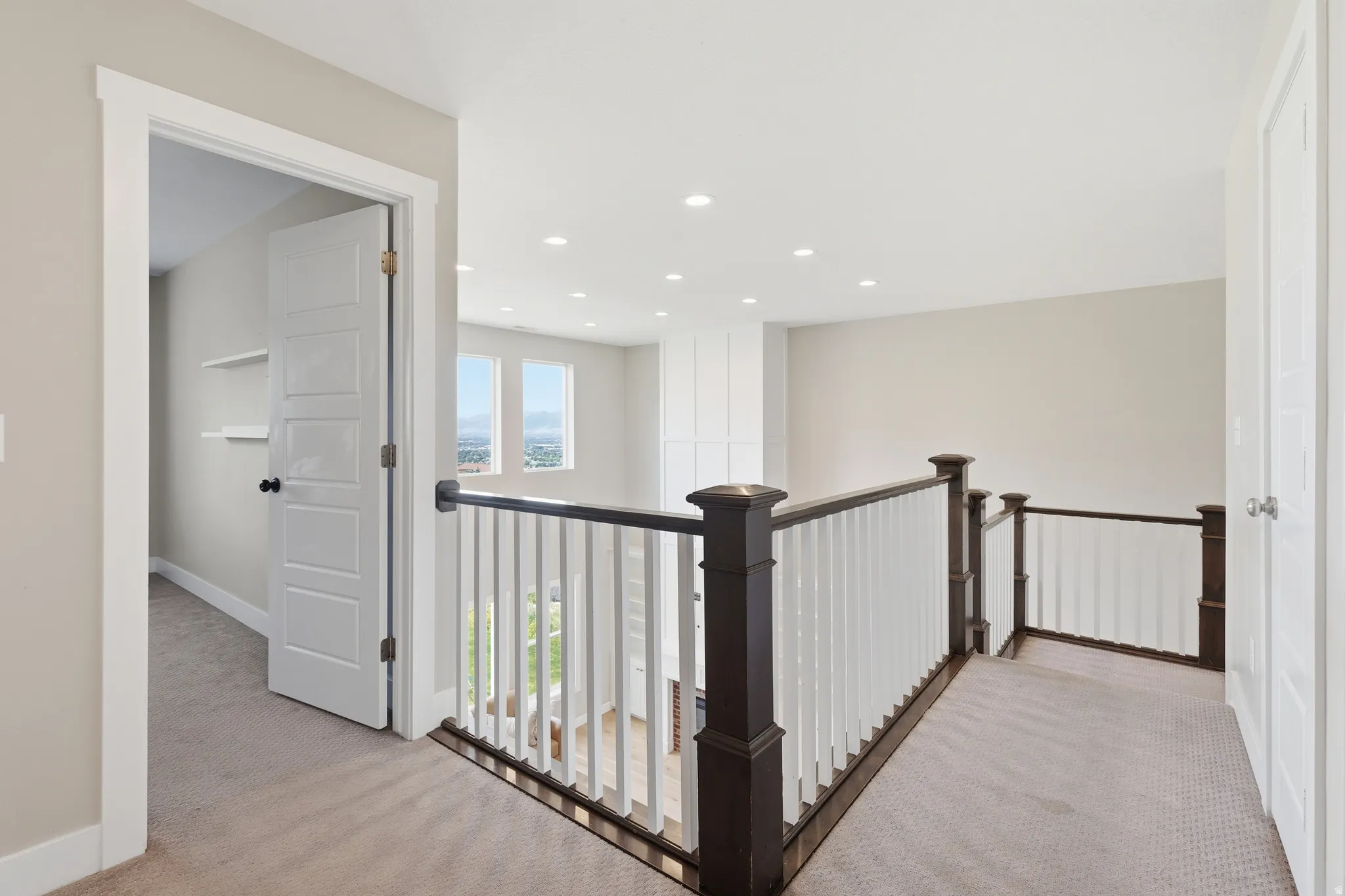 Carpeted landing featuring a dark wood newel post and balusters with white pickets, recessed lighting, and a paneled door