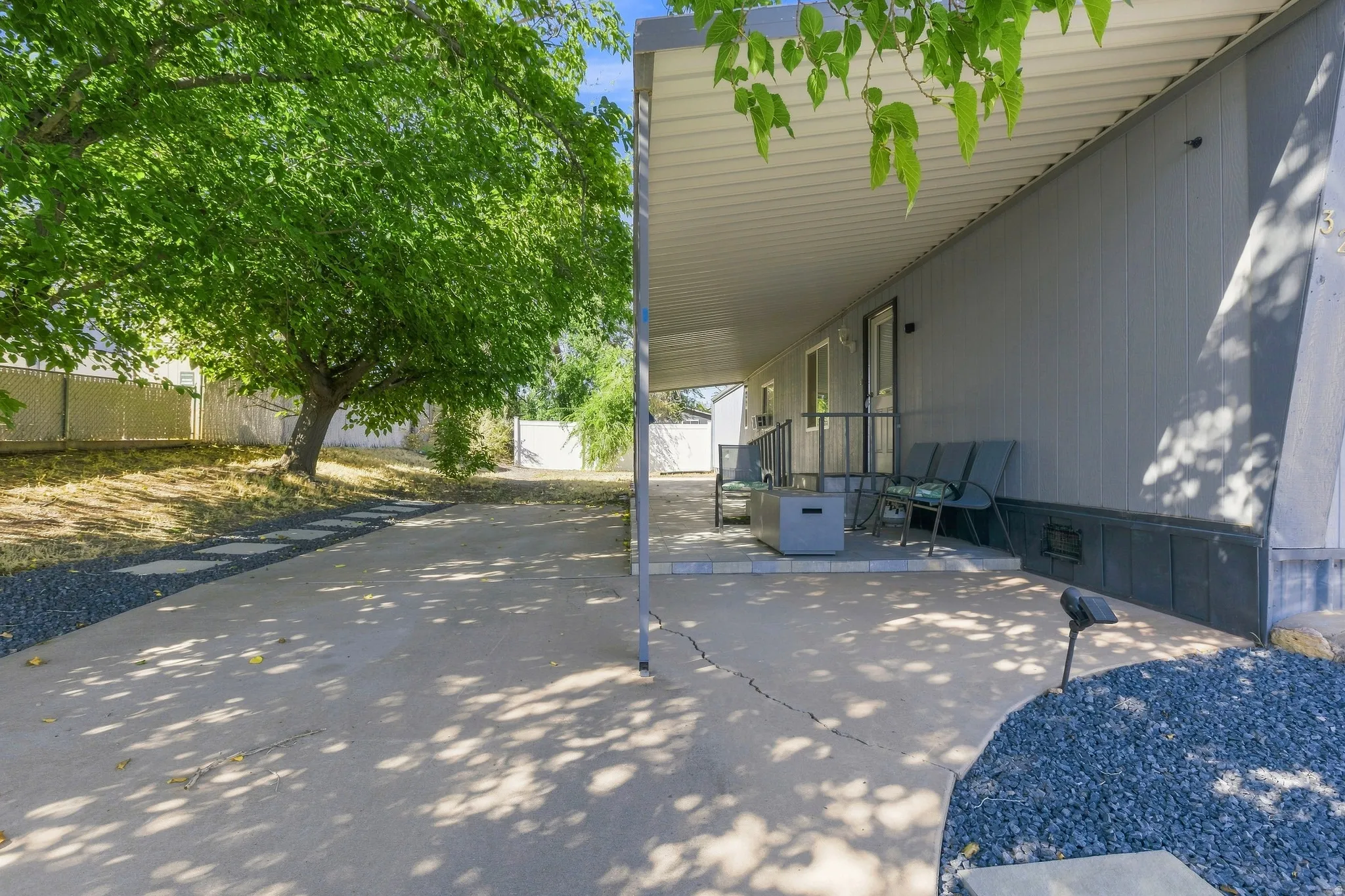 Expansive covered patio with concrete flooring, accented by a mature shade tree and a gravel pathway with stepping stones
