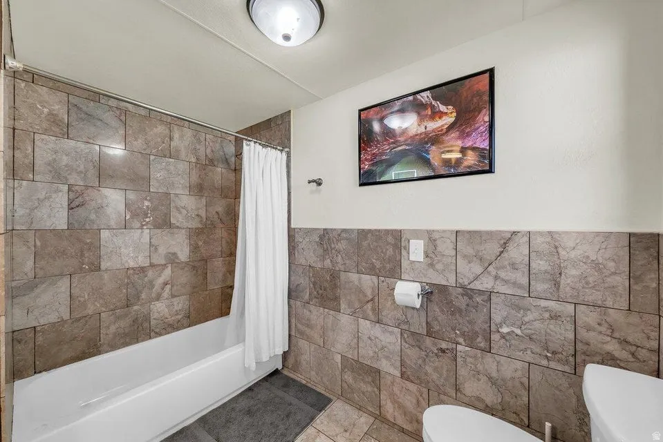 Bathroom featuring tile walls, shower / bath combo, tile patterned flooring, and a wainscoted wall