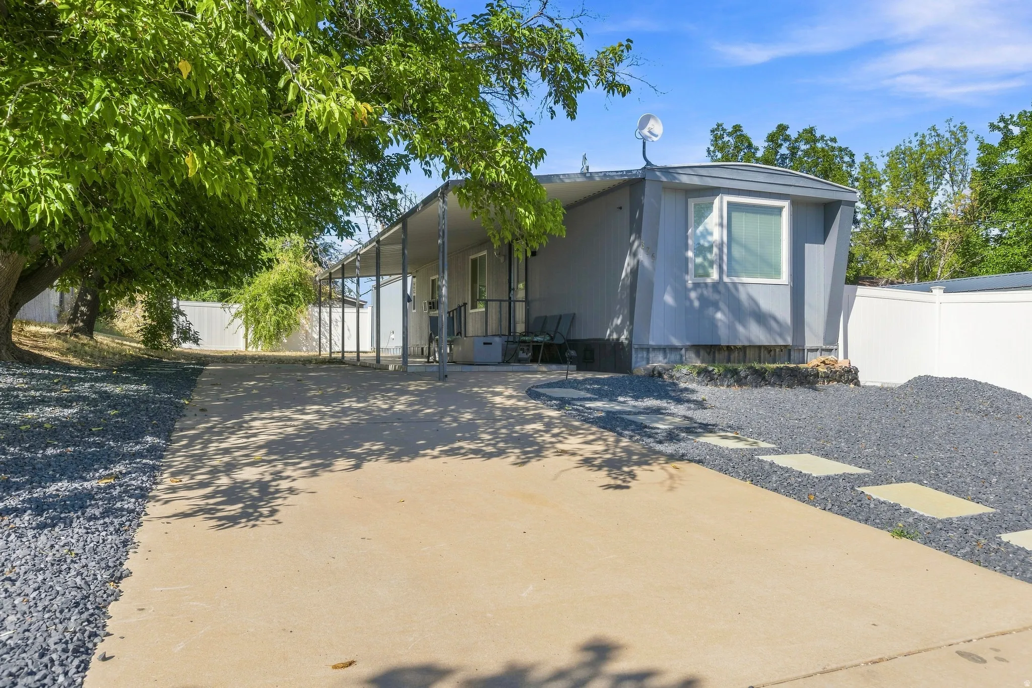 Expansive concrete driveway, gravel landscaping, white privacy fencing, and a covered porch