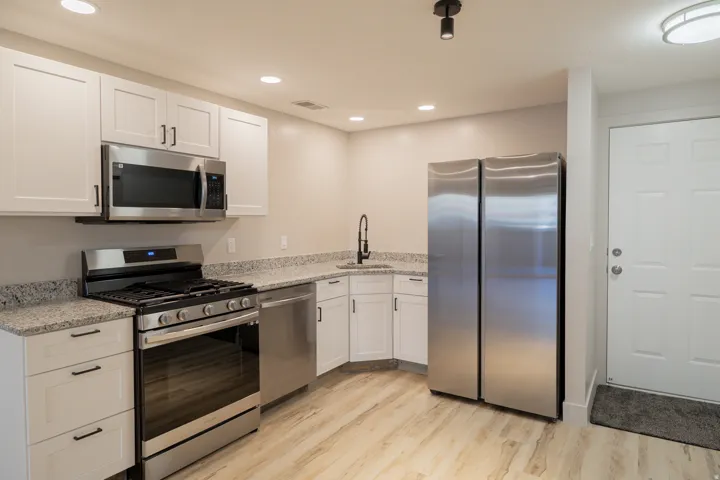Kitchen featuring stainless steel appliances, light stone countertops, white cabinets, light wood-style floors, and recessed lighting