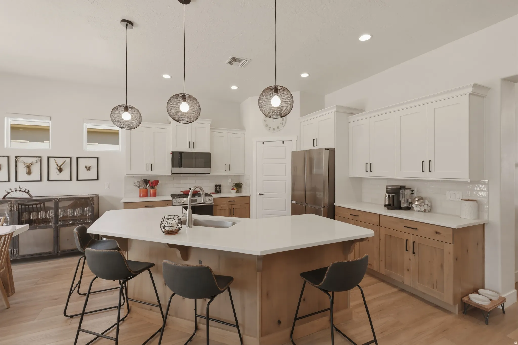 Kitchen featuring two tone cabinets, light wood finished floors, a kitchen bar, stainless steel appliances, and a center island with sink