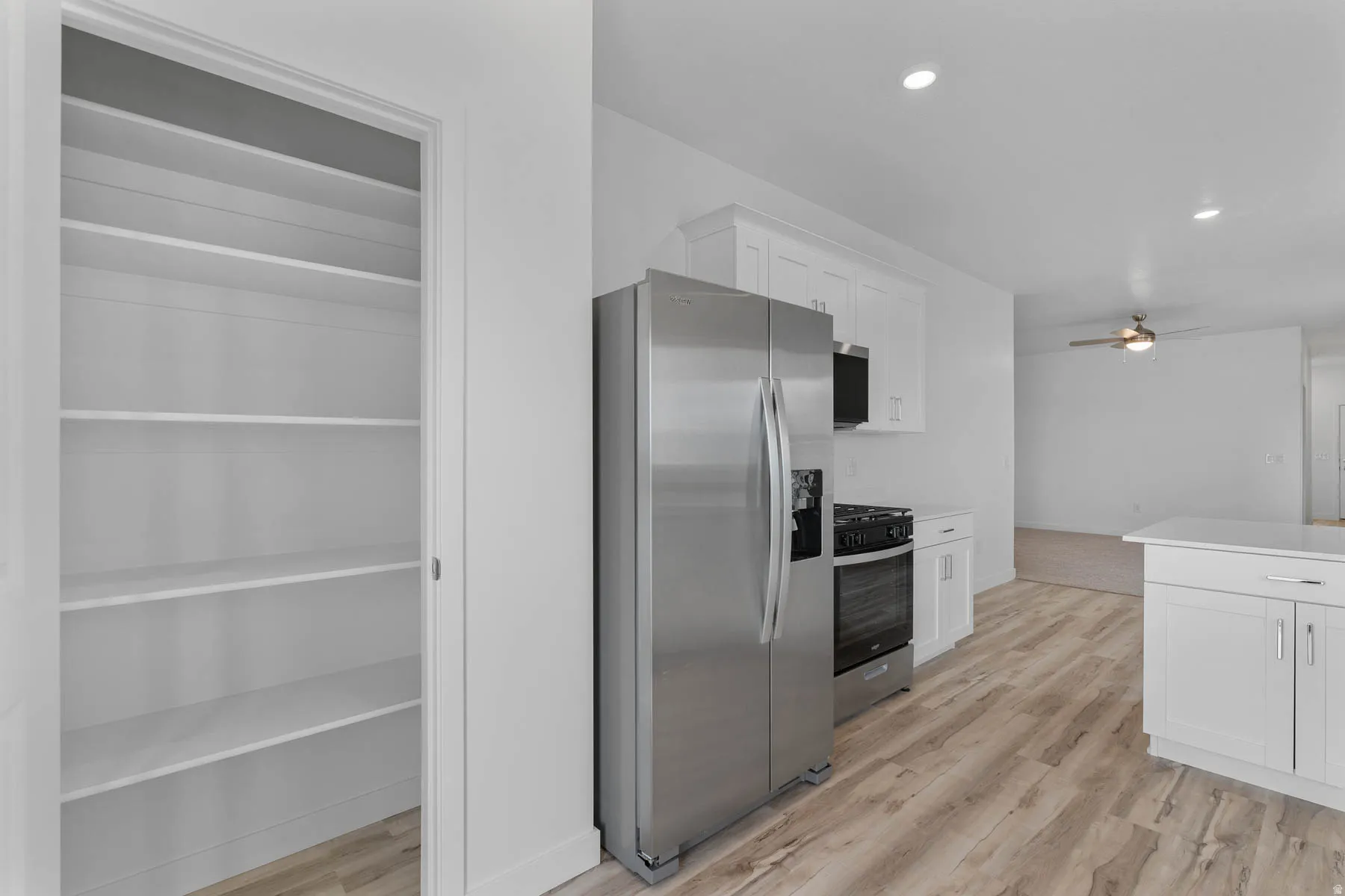 Kitchen pantry featuring multiple shelves for storage, stainless steel refrigerator, white cabinetry, integrated microwave, and wood-finish flooring