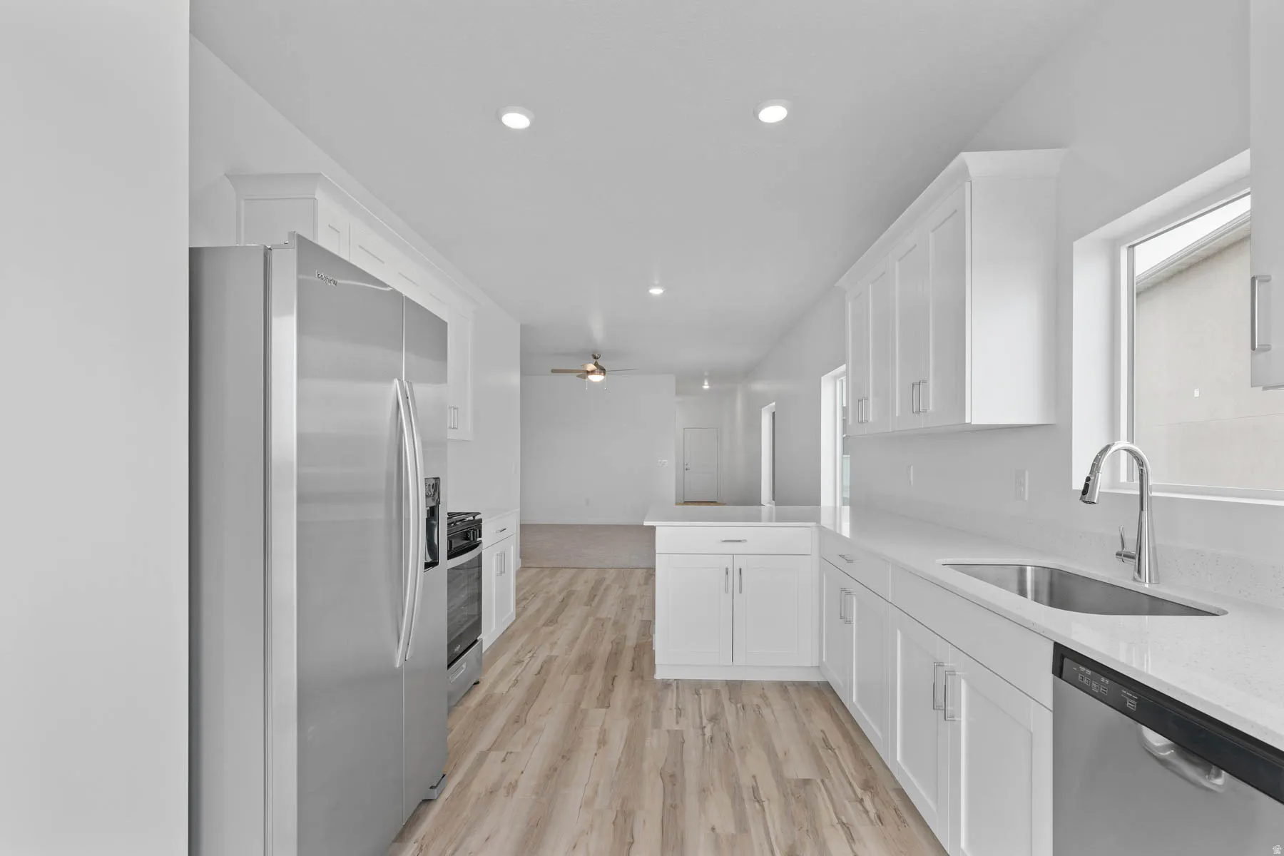 Contemporary kitchen featuring wood-finish flooring, white cabinetry, integrated stainless steel appliances, a stainless steel sink with a gooseneck faucet, and recessed lighting