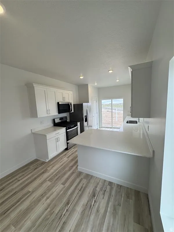 Kitchen with stainless steel appliances, a peninsula, light wood-style floors, white cabinets, and recessed lighting