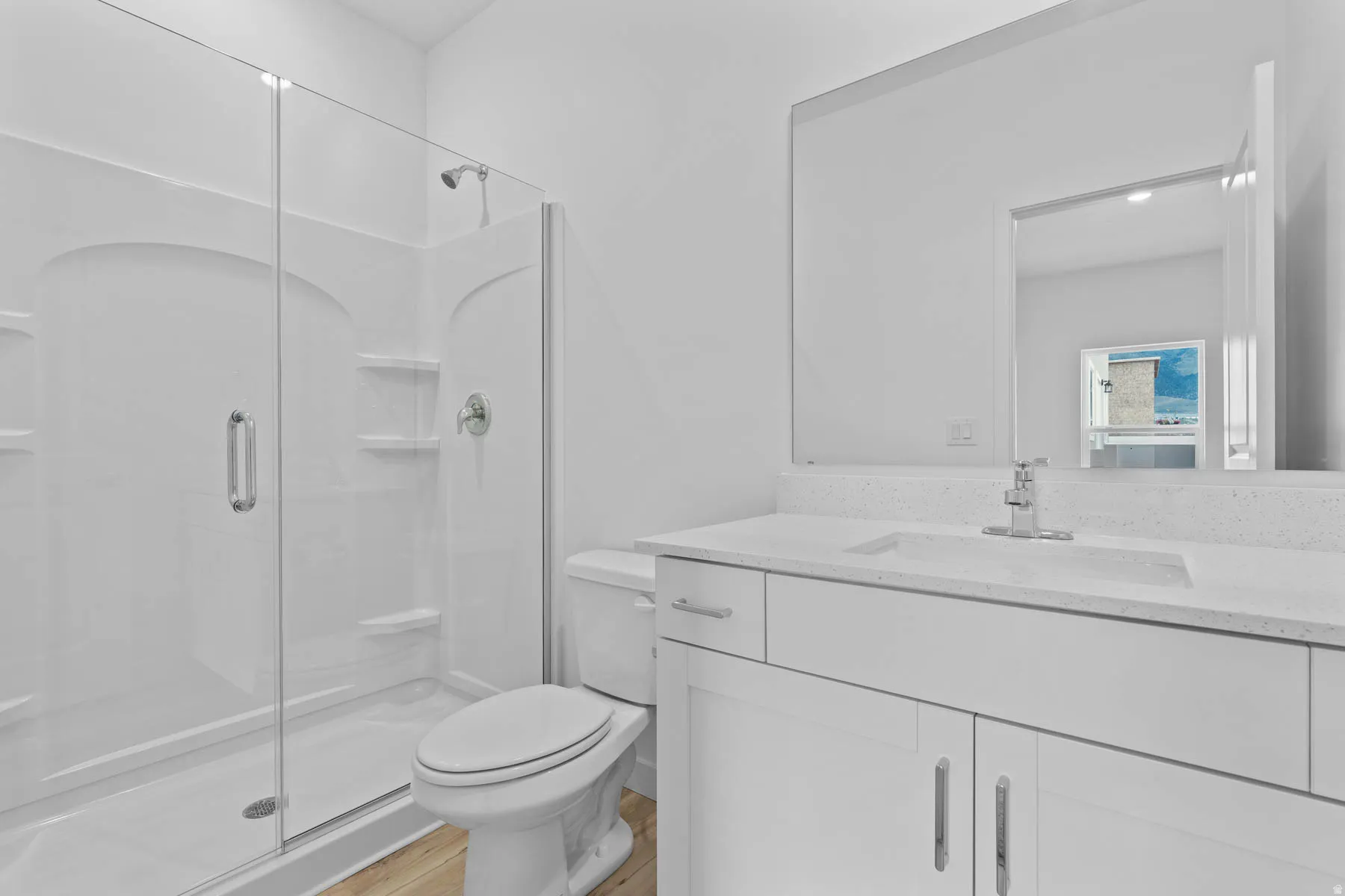 Bathroom featuring a glass-enclosed shower, white vanity with integrated sink, chrome fixtures, light-toned wood-finish flooring, and a large wall-mounted mirror
