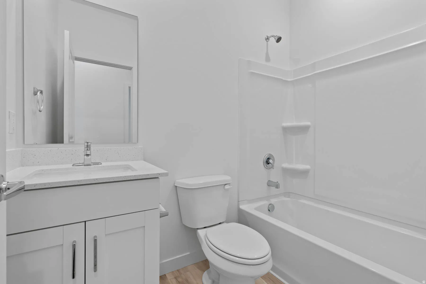 Bathroom featuring a white vanity with a light speckled countertop, an undermount sink, a chrome faucet, a white toilet, and a white tub with shower